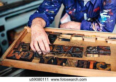 Stock Image - Senior craftsman reaching for wooden letterpress letters, mid section. Fotosearch