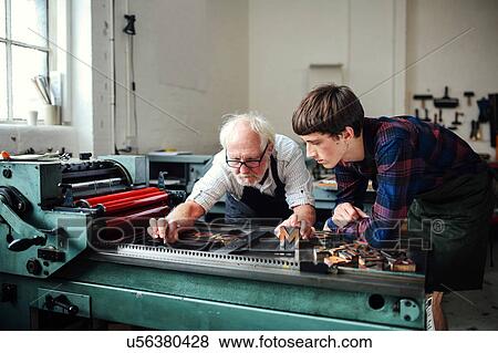 Senior craftsman teaching young craftsman to use letterpress machine in book arts workshop View Large Photo Image Stock Photo - Senior craftsman teaching young craftsman to use letterpress machine in book arts workshop. Fotosearch