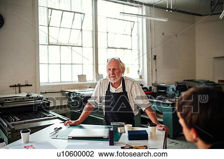 Stock Image - Senior craftsman/technician leading workshop in letterpress studio. Fotosearch