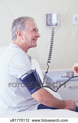 Stock Image - Senior male patient having blood pressure taken by doctor. Fotosearch