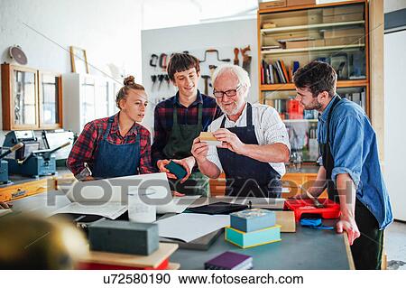 Stock Image - Senior male workshop leader showing materials to young group of men and women in book arts workshop. Fotosearch
