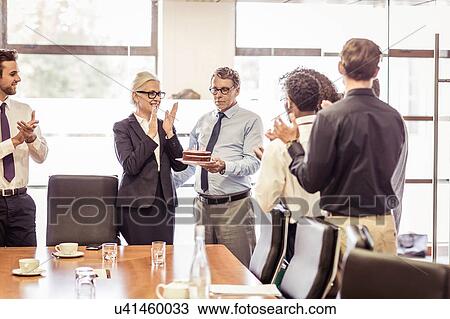 Stock Image - Senior man presenting cake with candles to business team in boardroom. Fotosearch
