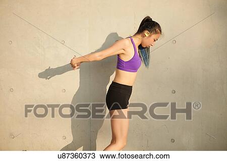 Stock Image - Side view of woman, hands behind back stretching. Fotosearch