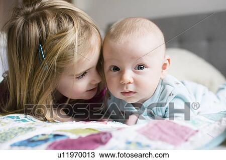 Stock Image - Sister (2-3) and brother (6-11 months) lying on bed. Fotosearch