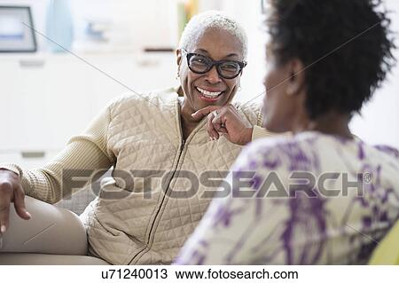 Stock Image - Smiling women sitting and talking in living room. Fotosearch
