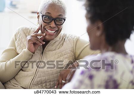 Stock Image - Smiling women sitting and talking in living room. Fotosearch