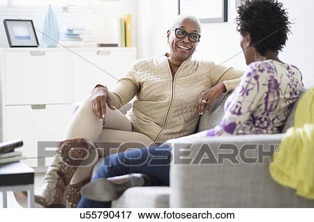 Stock Photo - Smiling women sitting and talking in living room. Fotosearch