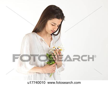 Stock Image - Studio portrait of young woman gazing at bunch of daisies. Fotosearch