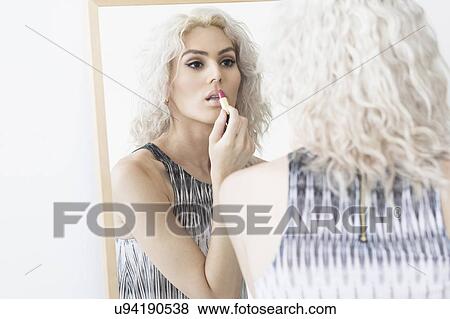 Stock Photo - Studio shot of young woman applying lipstick. Fotosearch