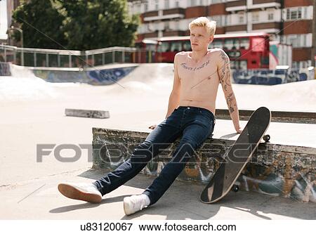 Stock Photo - Tattooed young male skateboarder sitting in skatepark. Fotosearch