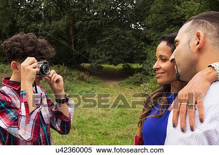 Stock Photography - Teenage boy photographing parents outdoors, using camera. Fotosearch