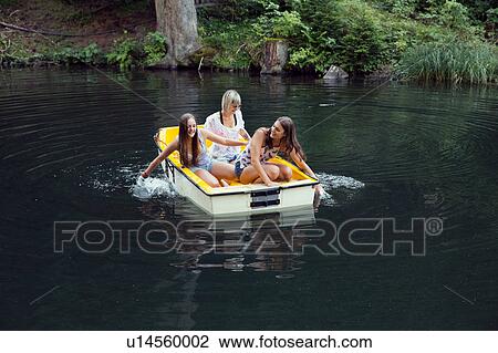 Stock Image - Three adult female friends hand paddling rowing boat on lake, Sattelbergalm, Tirol, Austria. Fotosearch