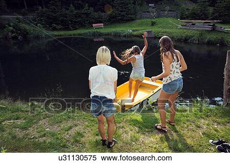 Stock Photography - Three adult female friends jumping into rowing boat on lake, Sattelbergalm, Tirol, Austria. Fotosearch