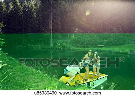 Stock Image - Three adult female friends launching rowing boat on lake, Sattelbergalm, Tirol, Austria. Fotosearch