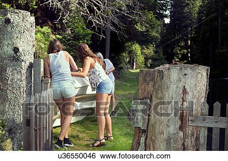 Stock Photograph - Three adult female friends moving rowing boat in garden. Fotosearch