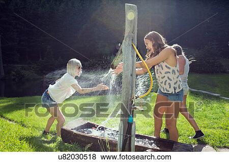 Three adult female friends play fighting sprinkling water hose in garden View Large Photo Image Stock Photo - Three adult female friends play fighting sprinkling water hose in garden. Fotosearch