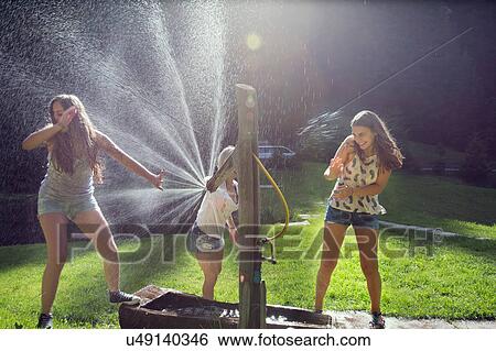 Three adult female friends play fighting sprinkling water hose in garden View Large Photo Image Stock Photograph - Three adult female friends play fighting sprinkling water hose in garden. Fotosearch