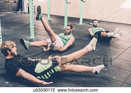 Stock Image - Three male cross trainers doing warm ups in gym. Fotosearch