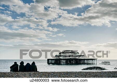 Stock Image - Tourists relaxing on Brighton beach, England. Fotosearch
