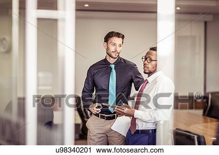 Stock Image - Two businessmen chatting in boardroom. Fotosearch