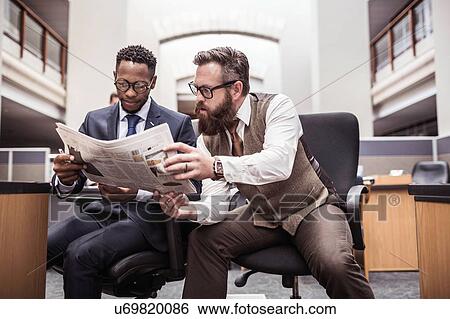 Two businessmen reading broadsheet newspaper in office View Large Photo Image Stock Photograph - Two businessmen reading broadsheet newspaper in office. Fotosearch