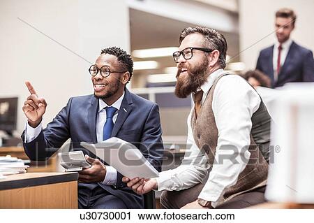 Two businessmen reading paperwork and pointing in office View Large Photo Image Stock Image - Two businessmen reading paperwork and pointing in office. Fotosearch