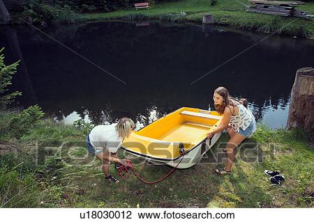 Stock Image - Two female friends manoeuvering rowing boat on lakeside, Sattelbergalm, Tirol, Austria. Fotosearch