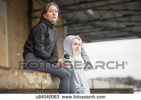 Stock Image - Two female runner friends looking out from warehouse platform. Fotosearch