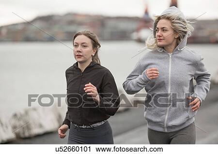 Stock Image - Two female runner friends running on dockside. Fotosearch