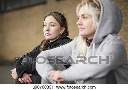 Stock Image - Two female runner friends sitting on warehouse platform. Fotosearch