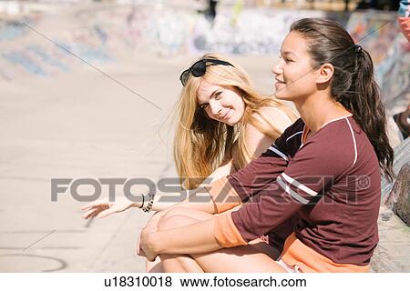 Stock Photo - Two female skateboarders sitting in skatepark. Fotosearch