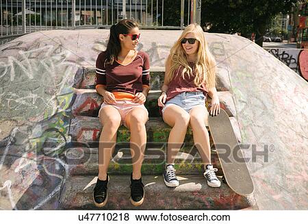 Stock Photo - Two female skateboarding friends chatting in skatepark. Fotosearch