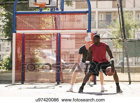 Stock Photograph - Two male basketball players practising on basketball court. Fotosearch