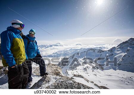 Stock Image - Two male snowboarders looking out over snow-covered landscape, Trient, Swiss Alps, Switzerland. Fotosearch