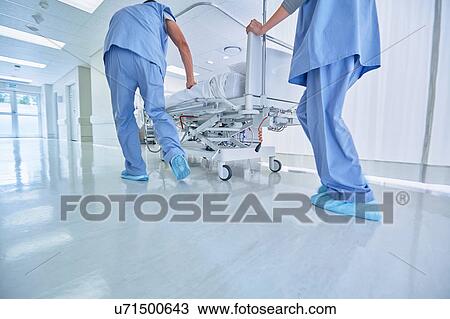 Stock Image - Two medics urgently pushing hospital bed in corridor. Fotosearch