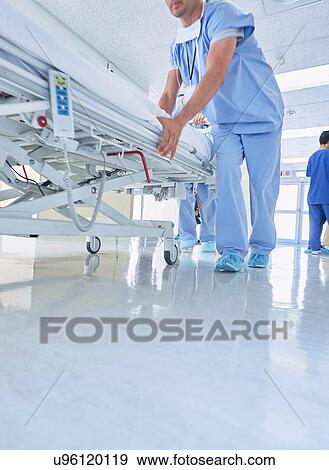 Stock Photo - Two medics urgently pushing hospital bed along corridor. Fotosearch