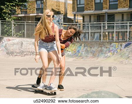Stock Image - Two women practising skateboarding balance in skatepark. Fotosearch