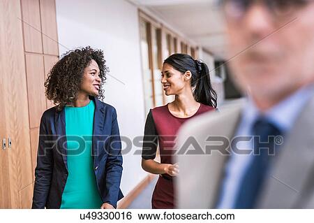 Stock Photograph - Two young businesswomen talking at office. Fotosearch