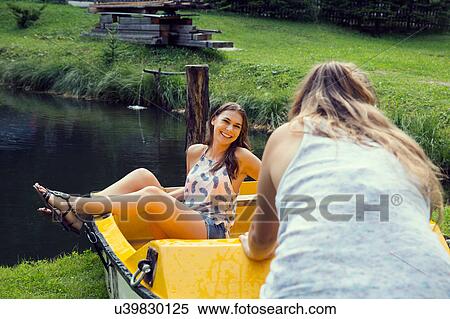 Stock Photography - Two young female friends pushing rowing boat at lakeside. Fotosearch