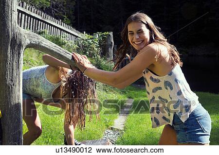 Two young female friends sprinkling water hose in garden View Large Photo Image Stock Image - Two young female friends sprinkling water hose in garden. Fotosearch