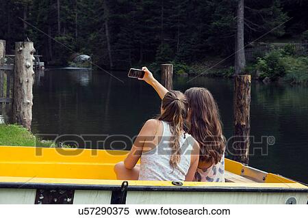 Two young female friends taking smartphone selfie in rowing boat, Sattelbergalm, Tirol, Austria View Large Photo Image Stock Photography - Two young female friends taking smartphone selfie in rowing boat, Sattelbergalm, Tirol, Austria. Fotosearch