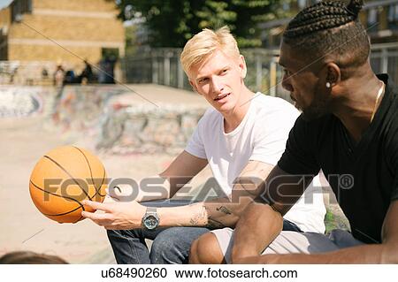 Stock Image - Two young male basketball players chatting in city skatepark. Fotosearch