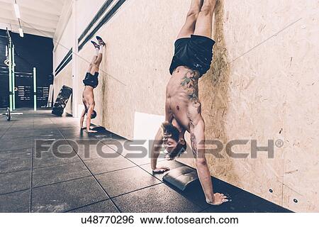 Two young male cross trainers doing handstands against gym wall View Large Photo Image Stock Photograph - Two young male cross trainers doing handstands against gym wall. Fotosearch