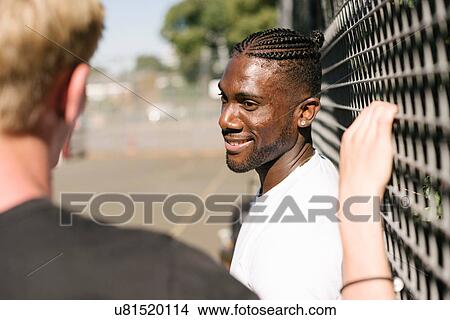 Picture - Two young men chatting by wire fence. Fotosearch