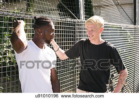 Two young men chatting by wire fence View Large Photo Image Stock Photograph - Two young men chatting by wire fence. Fotosearch