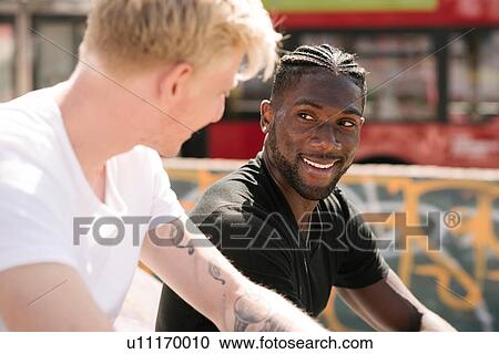 Stock Image - Two young men chatting in city skatepark. Fotosearch