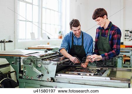 Stock Photo - Two young men working on letterpress machine in book arts workshop. Fotosearch
