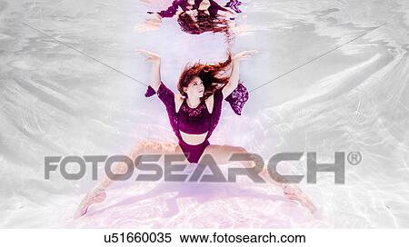 Stock Photography - Underwater view of girl wearing purple outfit and ballet shoes, feet pointed toward floor, arms raised. Fotosearch
