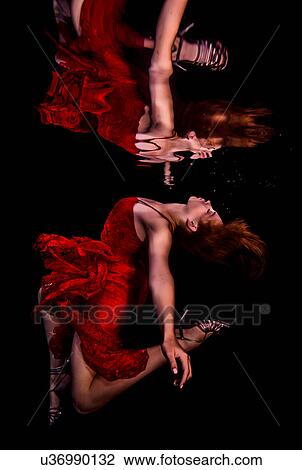 Stock Image - Underwater view of girl wearing red dress and high heeled shoes, reflected in water surface. Fotosearch