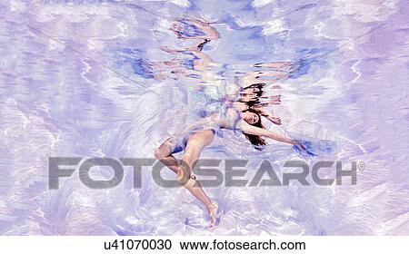 Stock Image - Underwater view of woman draped in sheer fabric, floating towards water surface. Fotosearch
